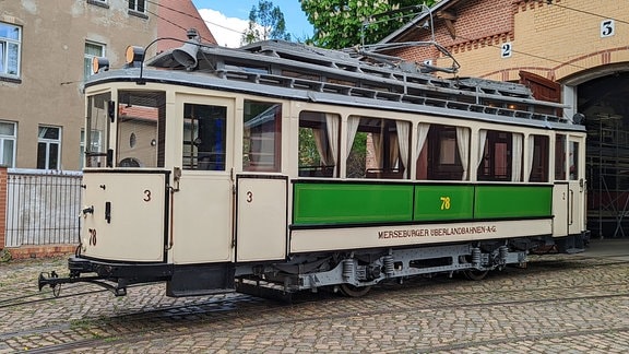 Ein historischer grün-weißer Triebwagen mit der Nummer 78 vor einem Straßenbahndepot.