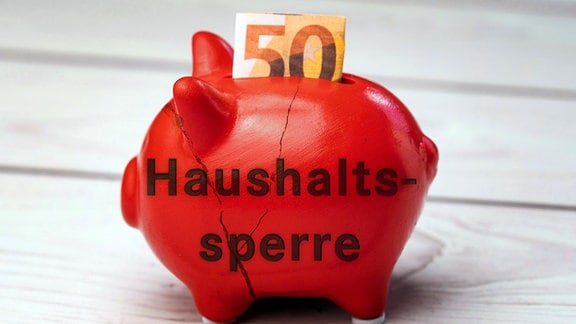 Budget-Lockdown-Schriftzug auf einem roten kaputten Sparschwein mit einer Euro-Banknote.