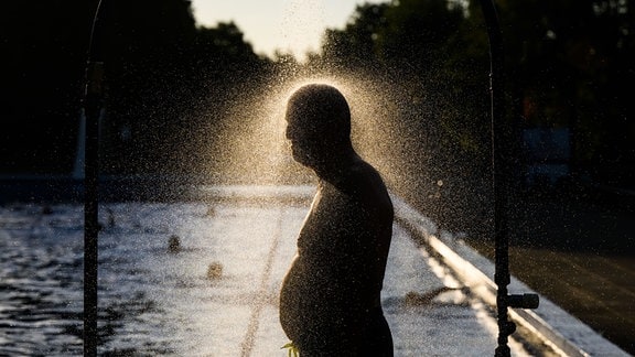 Ein Mann duscht am frühen Morgen im Freibad Annabad im Licht der aufgehenden Sonne.