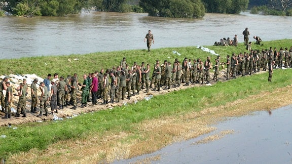 Soldaten und Soldatinnen der Bundeswehr und freiwillige Helfende sichern einen Deich. 