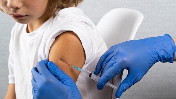 Einem kleinen Jungen wird eine Impfspritze in den Oberarm injiziert.