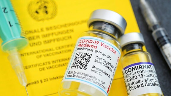 Impfausweis mit Impfspritzen und Impfstofffläschchen von Biontech und Moderna.
