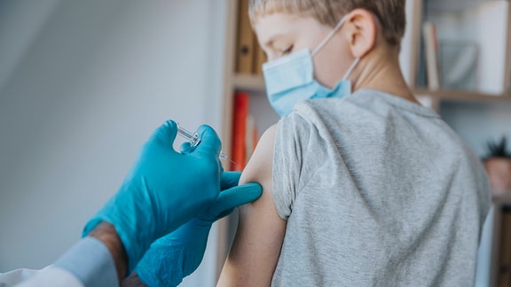 Junge mit Mundschutz erhält Impfspritze in den Oberarm.