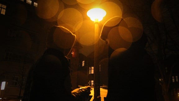 Zwei Jugendliche stehen im Dunkeln unter einer Straßenlaterne.
