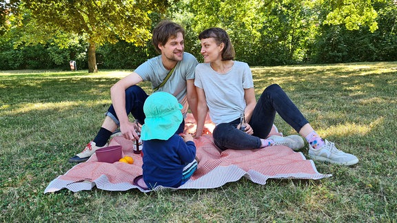 Glückliche Eltern sitzen mit ihrem Kind auf einer Decke.