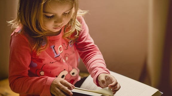 Ein Mädchen im Kindergartenalter schaut sich ein Buch an.