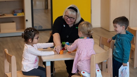 Kinder und eine Erzieherin spielen an einem Tisch.