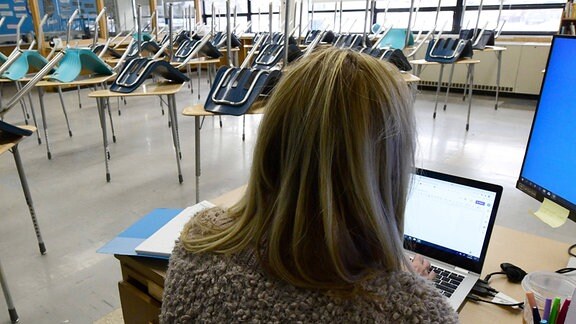 Eine Lehrerin sitzt im Klassenraum ohne Schüler