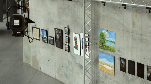 In einem lichtdurchfluteten Foyer hängen an Betonwänden - wie in einer Galerie - verschiedene Gemälde iund Fotografien dicht beieinander