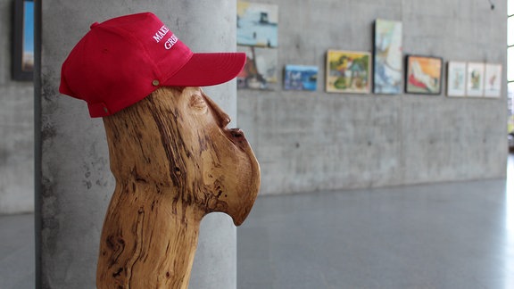 In einem lichtdurchfluteten Foyer hängen an Betonwänden - wie in einer Galerie - verschiedene Gemälde iund Fotografien dicht beieinander