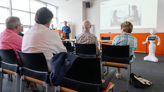 Menschen lauschen dem Vortrag eines jungen Mannes