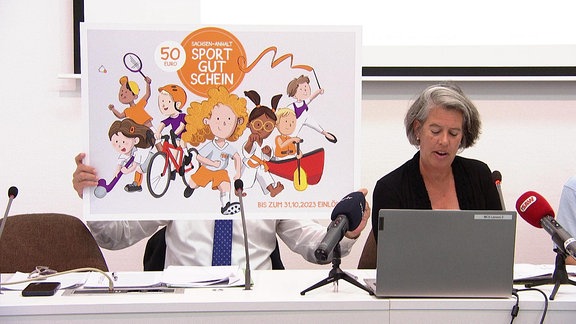 Ministerin Tamara Zieschang bei einer Pressekonferenz. Hinter ihr ein Plakat mit Kindern und der Aufschrift "Sportgutschein".