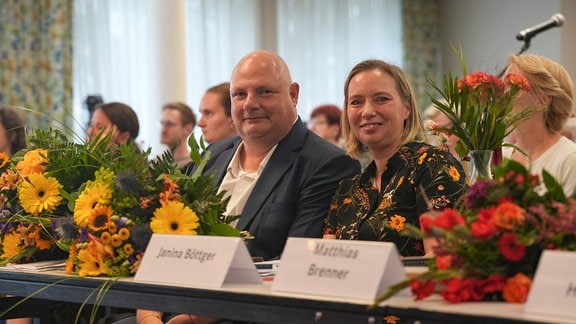 Janina Böttger und Hendrik Lange sitzen an einem Tisch, neben ihnen liegen Blumensträuße.