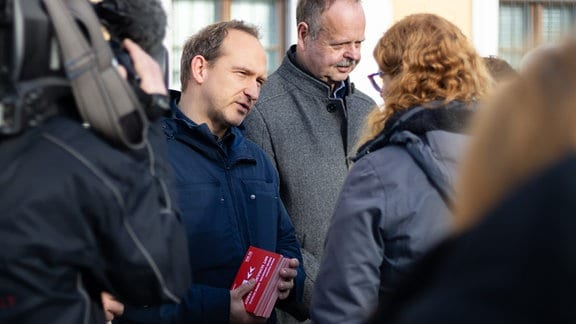 Der SPD-Landtagsabgeordnete Falko Grube spricht mit einer Frau. Er hält einen Stapel roter Postkarten in den Händen.