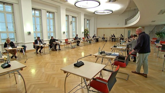 In einem Saal des Landtags Sachsen-Anhalt sitzen mehrere Menschen an einzelnen Tischen