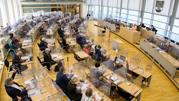 Der Plenarsaal des Landtags in Sachsen-Anhalt. Die Abgeordneten sitzen an ihren Tischen und stimmen mit Handzetteln ab. Durchsichtige Scheiben trennen die einzelnen Plätze voneinander.