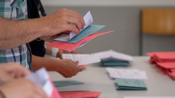 Wahlhelfer und Wahlhelferinnen öffnen im Klassenzimmer einer Schule in Magdeburg die Umschläge der Briefwahl. Diese liegen stapelweise nach Farben sortiert vor ihnen auf dem Tisch.