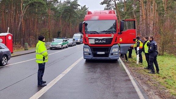 Ein Polizist beugt sich zu den Rädern eines Lkw herunter.