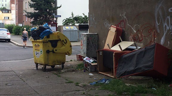 An einer Straßenecke stapelt sich der Müll: Eine Tonne quillt über, alte Möbelteile liegen herum