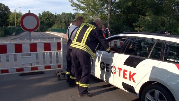 Zwei Feuerwehrmänner sprechen mit einem Autofahrer