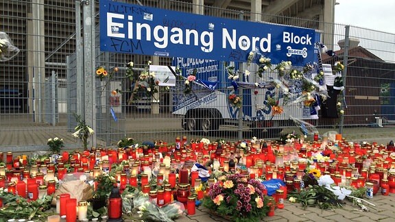 Vor dem Stadionszaun stehen Kerzen und Blumen