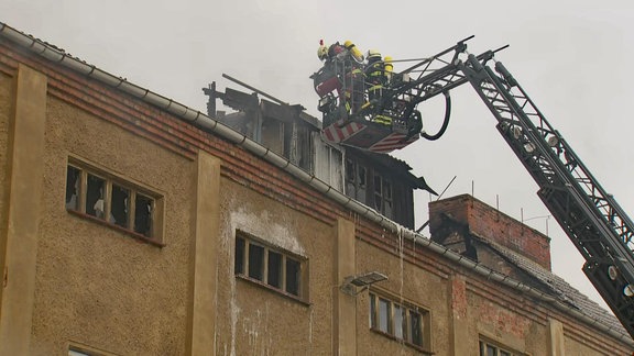 Aus dem Dachstuhl eines Gebäudes in Osterweddingen dringt dichter Rauch, eine Drehleiter der Feuerwehr ist zu sehen.