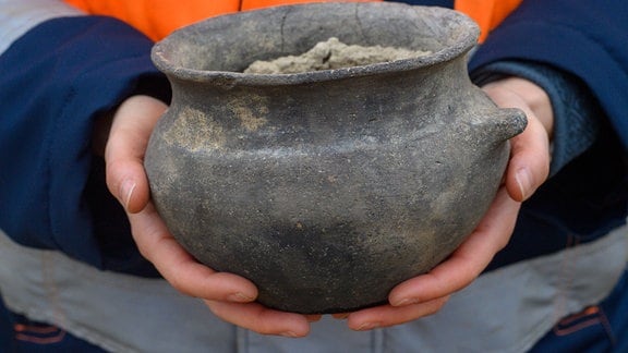 Anja Tuschwitz, Grabungsleiterin vom Landesamt für Denkmalpflege und Archäologie (LDA) Sachsen-Anhalt zeigt auf der Grabungsfläche ein Keramikgefäß aus der Frühbronzezeit das sie und ihr Team in einem bronzezeitlichen Brunnen entdeckt hat. 