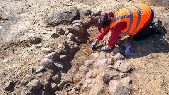 Eine Mitarbeiterin vom Landesamt für Denkmalpflege Sachsen-Anhalt arbeitet an einem Steinkistengrab aus der Eisenzeit