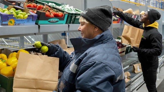 Innenaufnahme: zwei Personen packen Obst und Gemüse in Papiertüten.