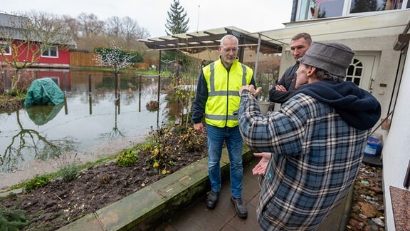 Drei Männer stehen beim Hochwasser der Ohre zu Weihnachten 2023 vor einem überfluteten Garten.