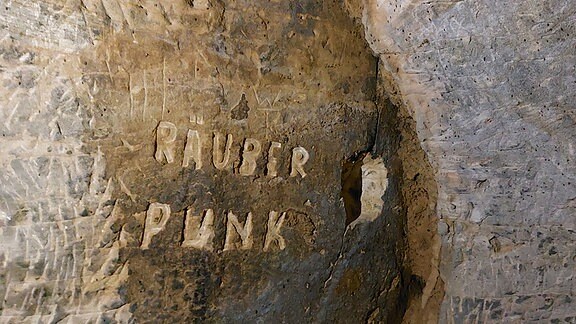 In eine Sandstein-Wand sind die Buchstaben RÄUBER PUNK geritzt