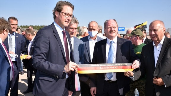 Landesverkehrsminister Webel und Bundesverkehrsminister Scheuer halten ein Stück Band in den Händen