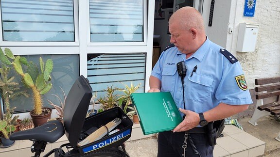 Der Polizist Dirk Böschel steht neben seinem Dienstfahrrad und schaut in den aufgeschraubten Koffer.