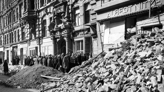 Menschen stehen nach der Kapitulation 1945 in den Ruinen Magdeburgs vor einem Lebensmittelgeschäft Schlange.