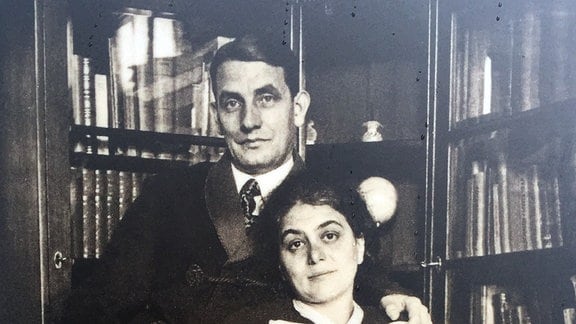 Ein historisches Foto zeigt ein Ehepaar, das auf einem Sessel vor einem Bücherregal posiert