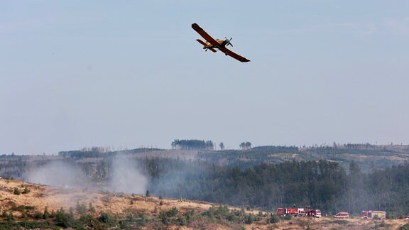 Ein Löschflugzeug ist über einem Waldgebiet im Einsatz.