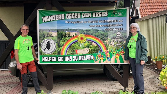 Ein älteres Ehepaar steht neben einem Plakat mit der Aufschrift "Wandern gegen den Krebs"