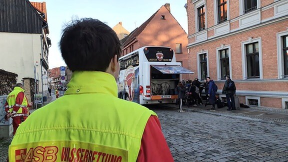 Ein Rettungssanitäter steht vor einem Schulbus mit Kindern. 