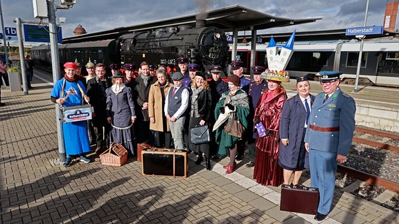 Teilnehmer einer Sonderfahrt einer alten Dampflok stehen in historischen Uniformen auf dem Bahnhof Halberstadt.