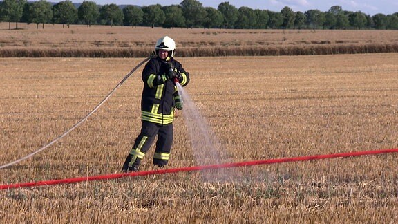Ein Feuerwehrmann in Schutzkleidung wässert ein Stoppelfeld.