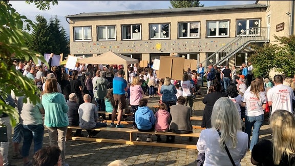 Viele Menschen befinden sich mit Plakaten vor einer Schule.