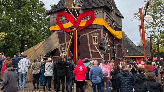 Besucher*innen tummeln sich vor einem eigenartigen Haus in einem Erlebnispark.