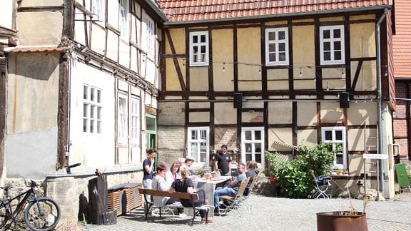 Auf dem Gut Ziegenberg in Ballenstedt stehen ein Fachwerkhaus, vor dem mehrere Menschen an einem Tisch sitzen und essen. 