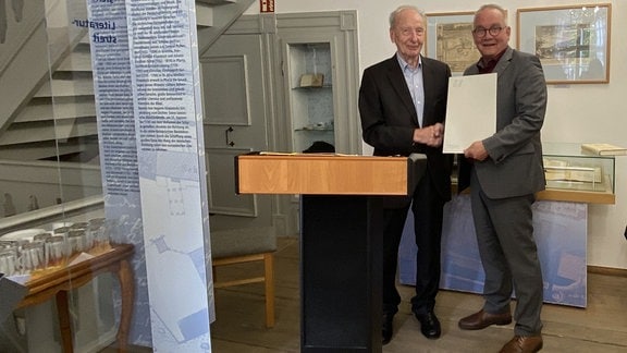 Der Quedlinburger Ehrenbürger Jürgen Weitkamp mit Oberbürgermeister Frank Ruch: Zwei Männer in Anzügen stehen in einem Museumsraum mit einer Mappe in der Hand 