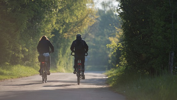 Zwei Fahrradfahrer fahren im Morgenlicht auf einem Weg.