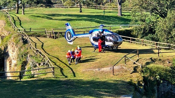 Rettungskräfte tragen einen Verletzten, im Hintergrund ein Helikopter