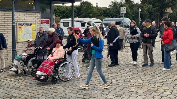 Eine Gruppe Menschen, zwei im Rollstuhl, laufen auf einem Weg in der Stadt.