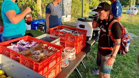 Eine Frau steht unter einem Pavillon an einem Stand mit Essen und trinkt 