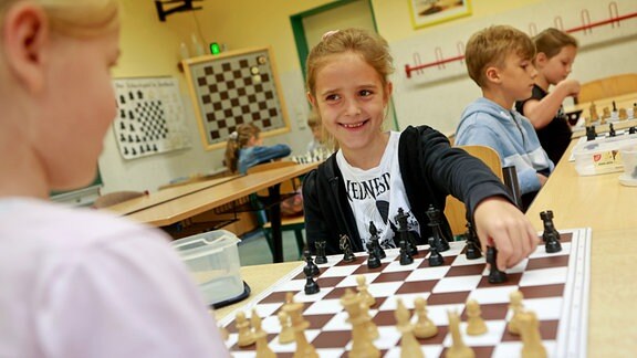 Schulkinder sitzen im Klassenraum und spielen Schach.