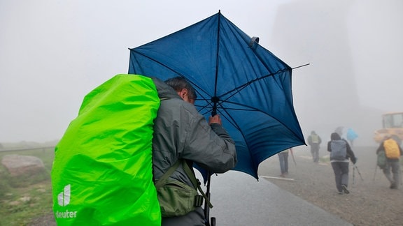 Mit einem Regenschirm ist ein Wanderer auf dem Brocken unterwegs.